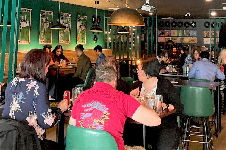 People are seated at tables indoors at a restaurant in conversation during a trivia event.