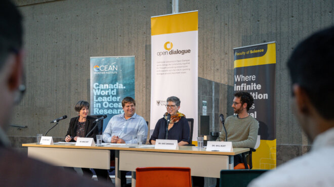 Four panelists sit at a table with microphones in front of decorative banners.