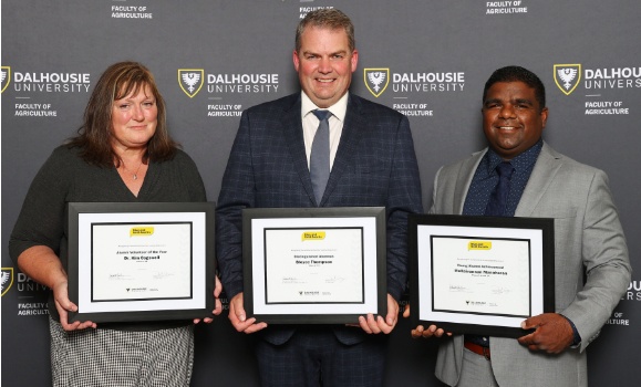 Three people hold framed certificates in front of them smiling and wearing business casual attire at an event. 