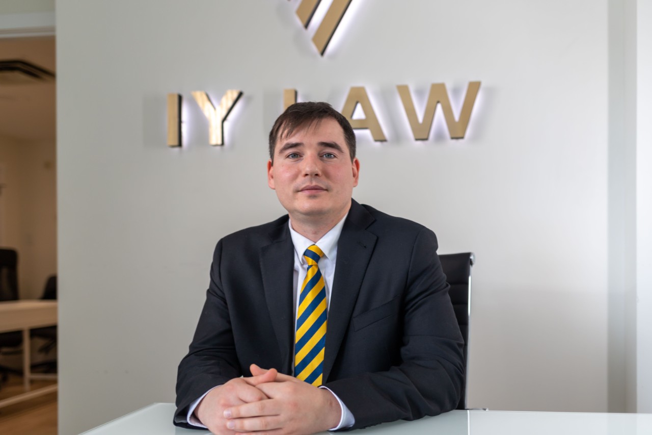 Yushchenko sits at a desk in his law firm with his hands clasped and smiling slightly in a suit and tie. 