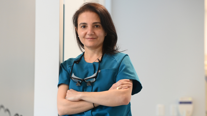  Nada Haidar has her arms folded and smiles slightly dressed in medical attire.