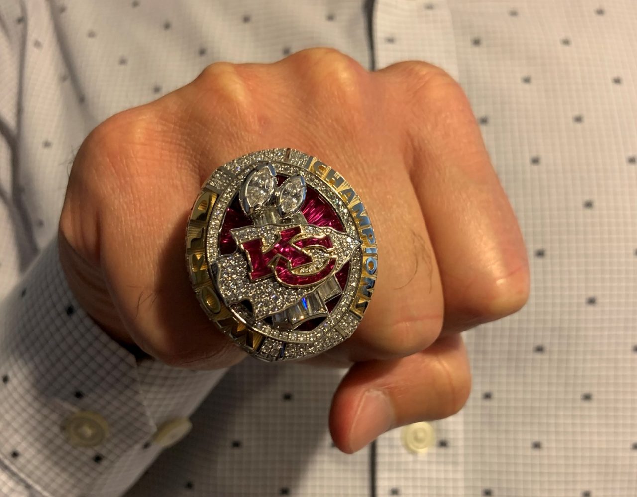 A Kansas City Chiefs Super Bowl ring displayed on a man's hand with his torso in the background.