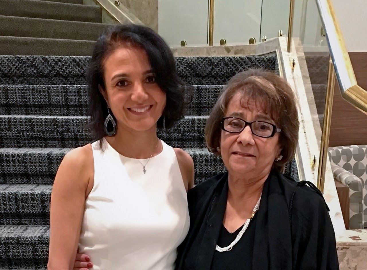 Haidar and her mother dressed semi-formally and smiling. in front of a staircase.