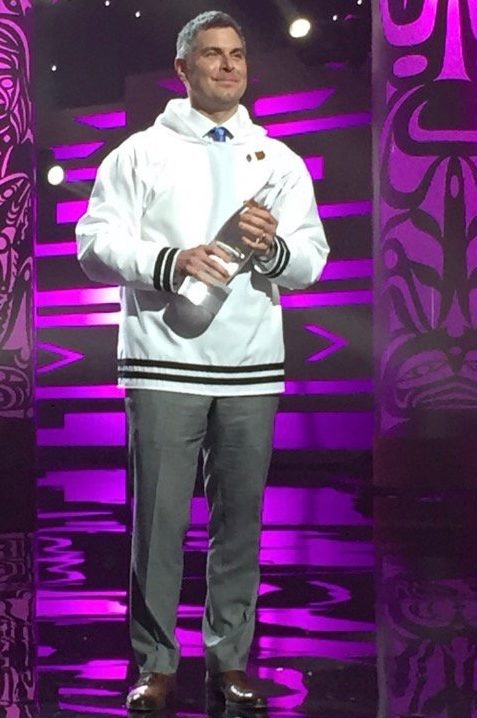Person on stage holding an award at an event with purple lighting and Indigenous-inspired designs.