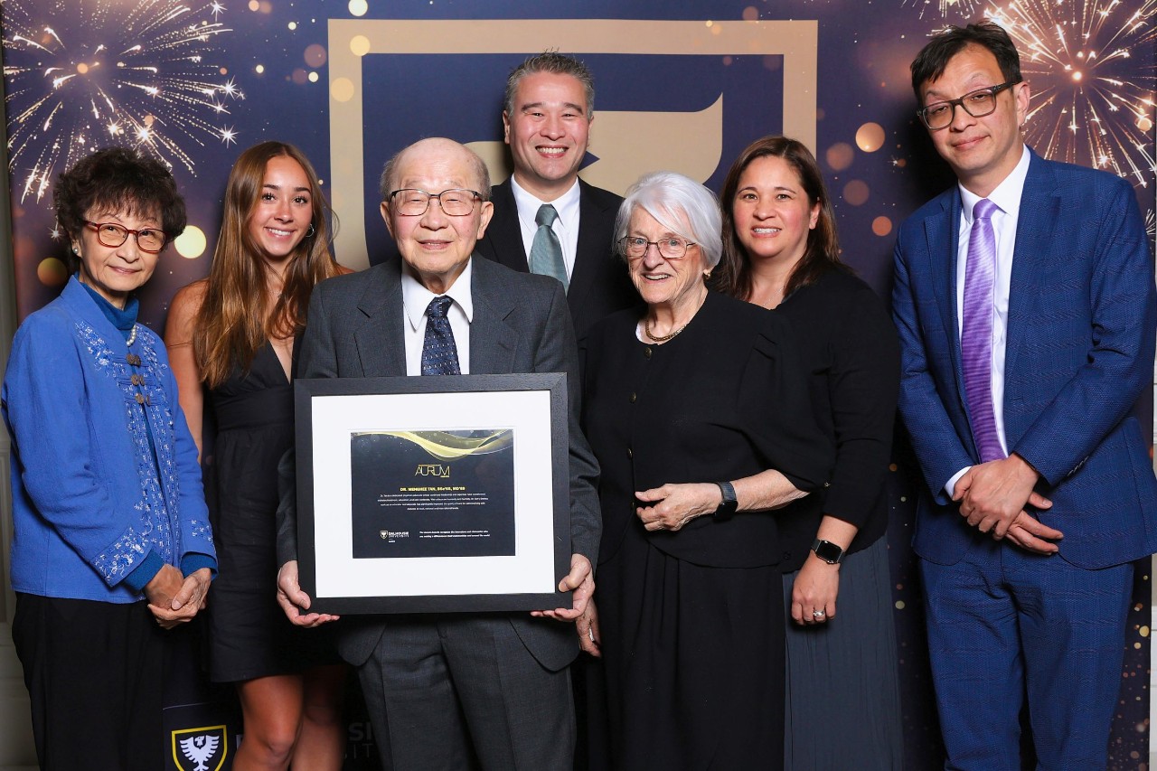 A man holds a framed certificate surrounded by a group of family members smiling at a semi-formal event.