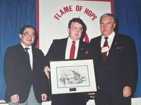 Three people at a “Flame of Hope” ceremony holding a framed presentation in 1989, marking a diabetes awareness initiative.
