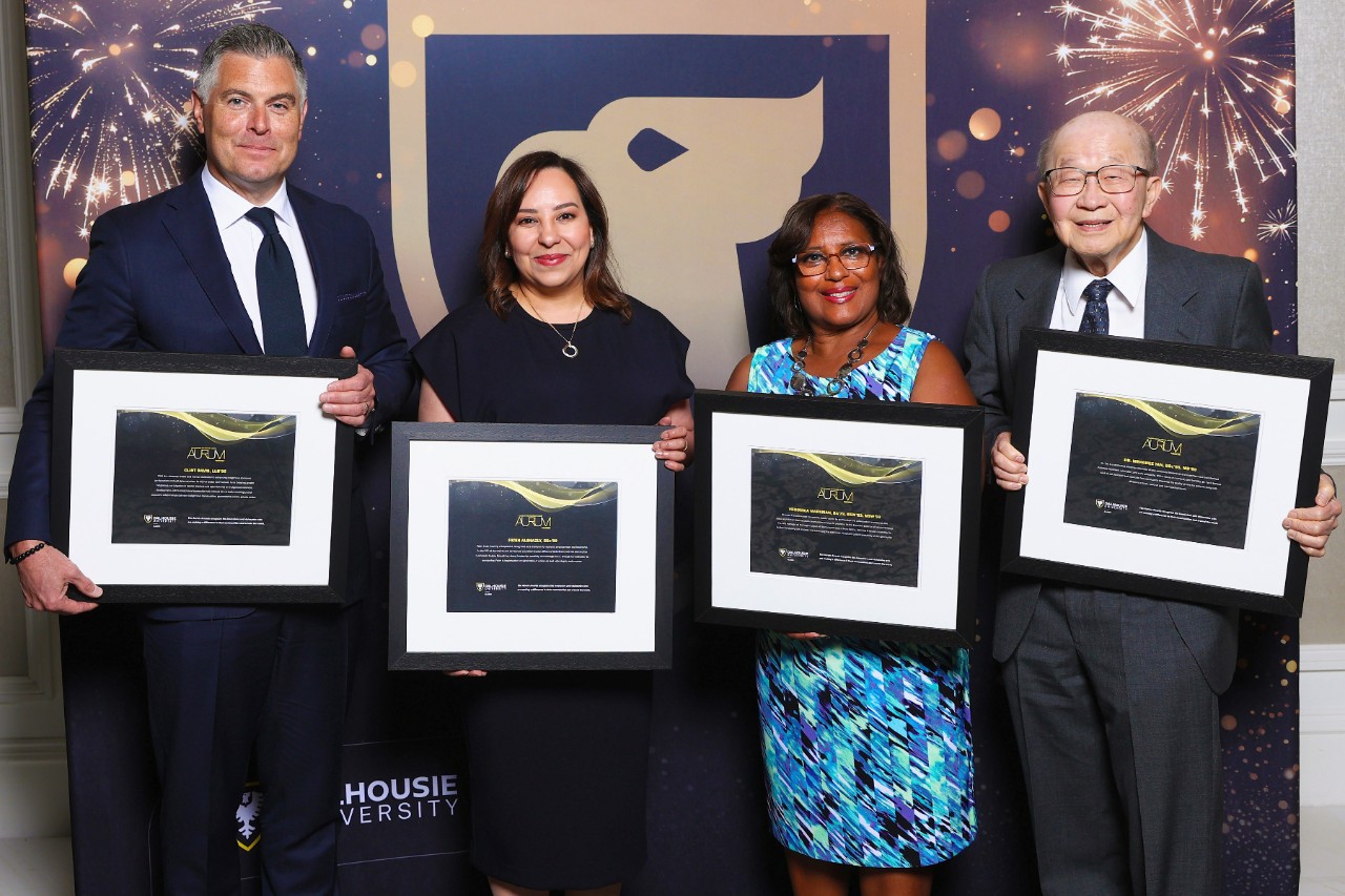 Four people stand holding framed certificates at a semi-formal event celebrating their awards.