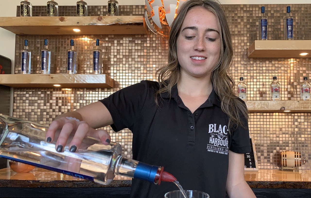 Landry pours from a spirits bottle behind the bar at Black Harbour Distillers.
