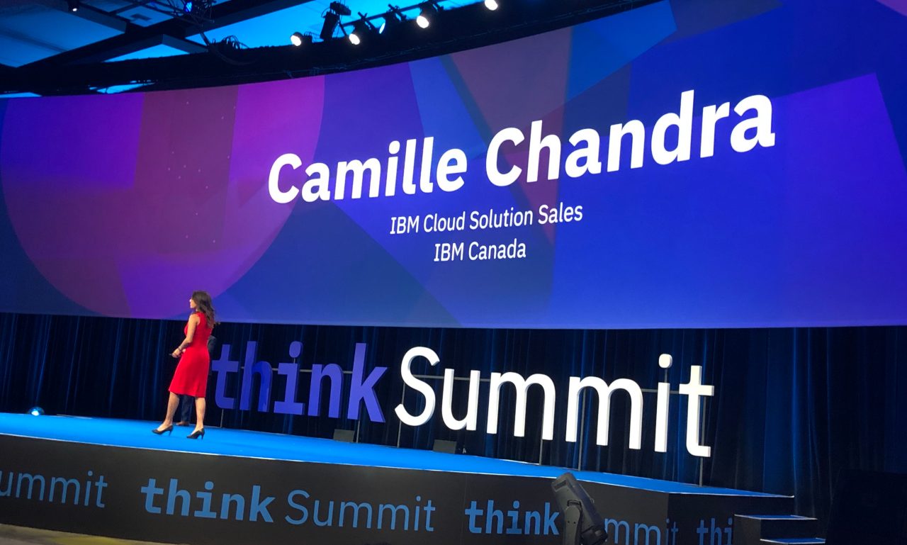 A woman in a red dress walks across a stage with a very wide screen as the backdrop.