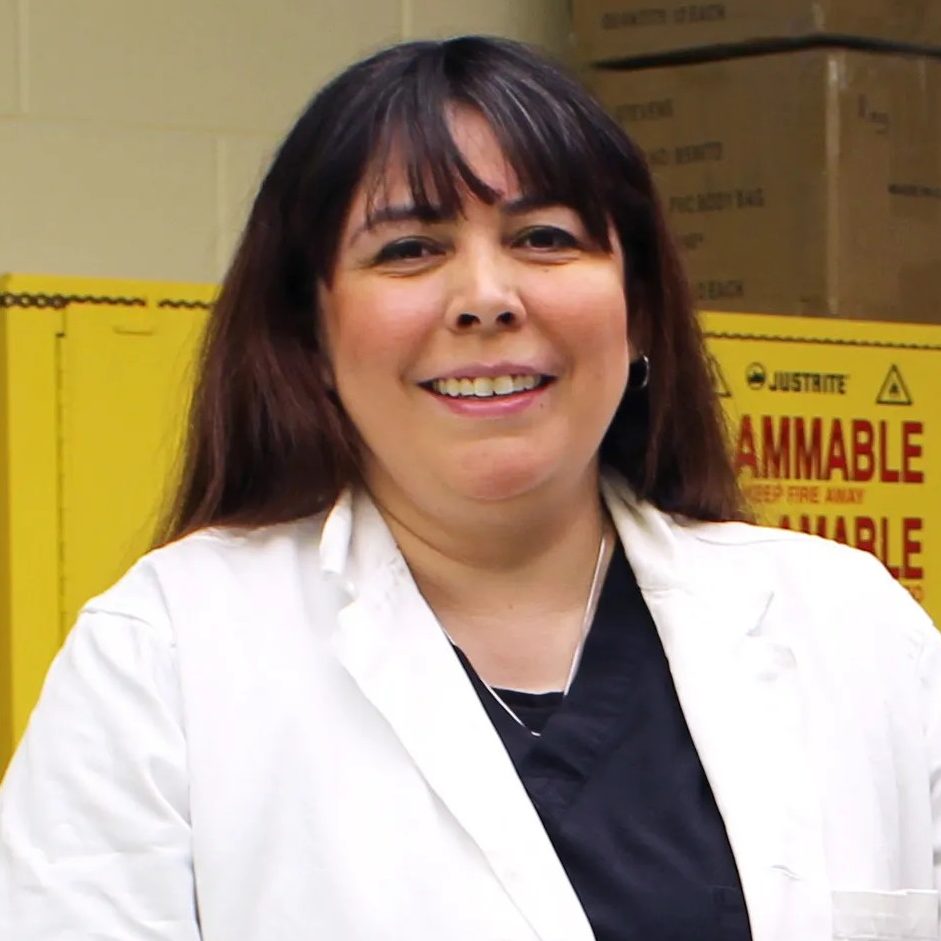 A woman in a white lab coat smiling in a lab. 