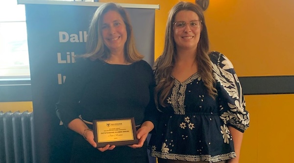 Two women stand together at a casual indoor event, one holding a small plaque.