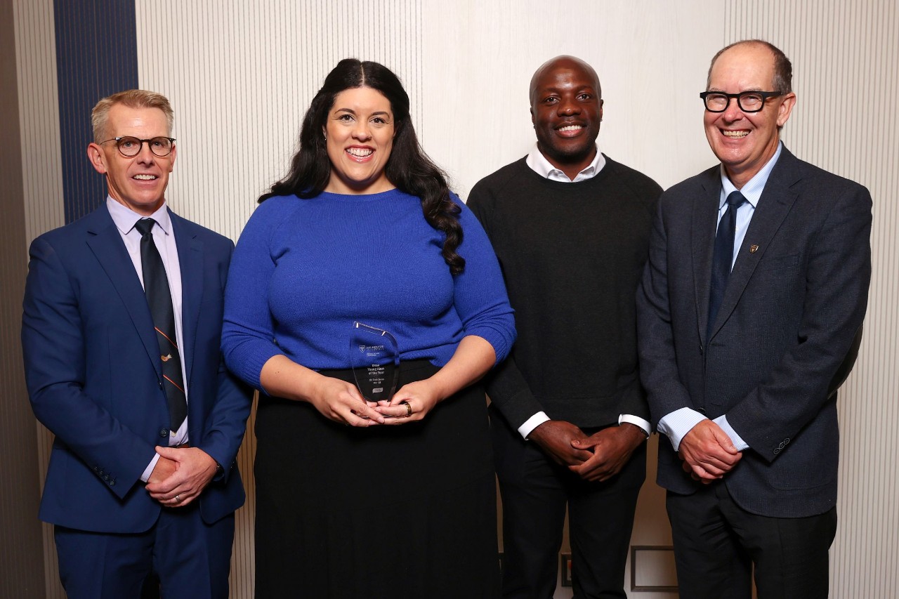 A woman stands holding a crystal award smiling among three men at an event.