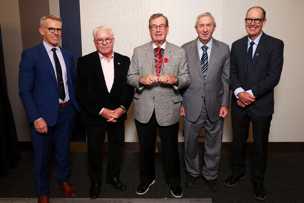 A man stands holding a crystal award smiling between four other men. 