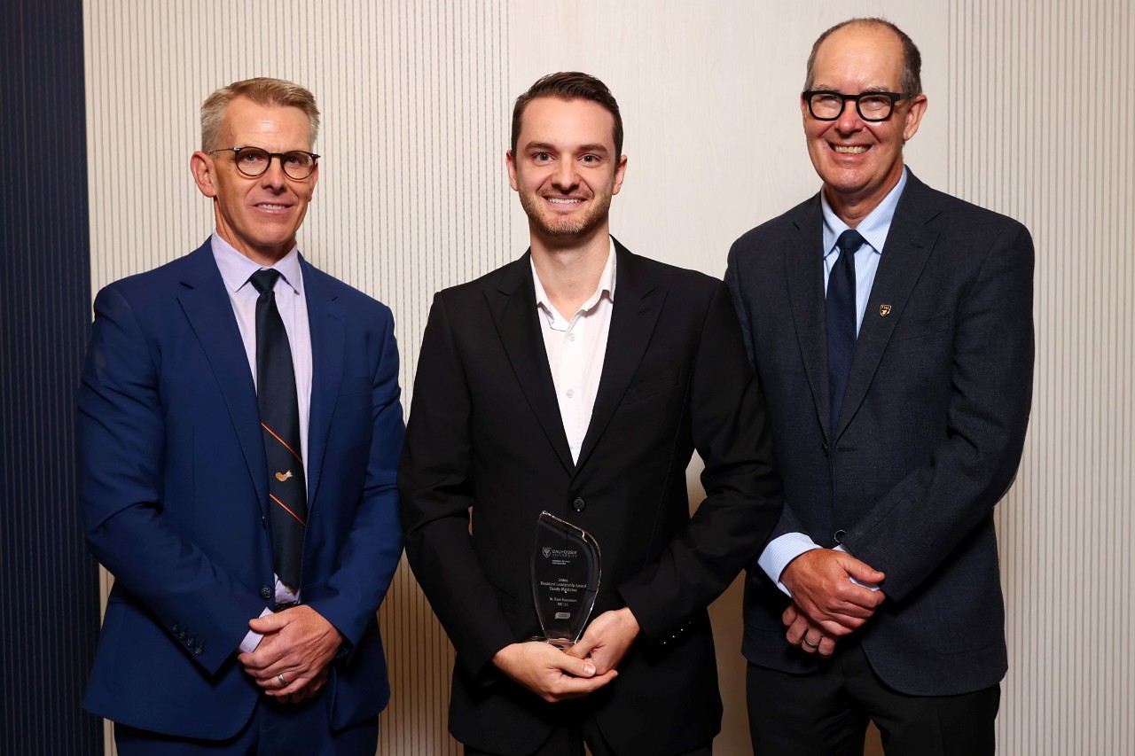 A man stands holding a crystal award smiling between two other men.