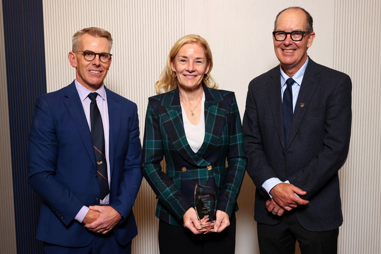 A woman stands holding a crystal award smiling between two men at an event. 