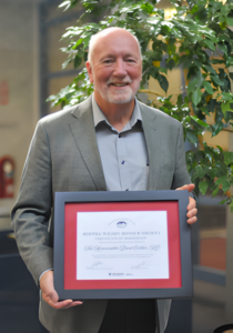 Brent Cotter stands holding a framed certificate at an event.