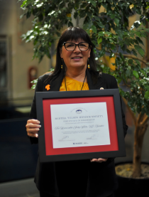 Judy White stands holding a framed certificate at an event.