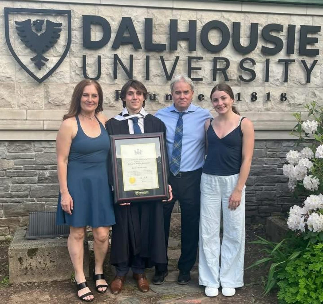 A family of four stands together in front of the Dalhousie University sign on graduation day.