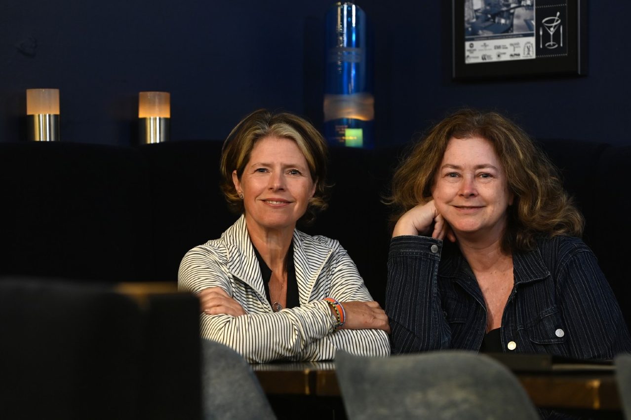 Lisa Murphy and Karen Spaulding leaning against a bar top in a restaurant, smiling.