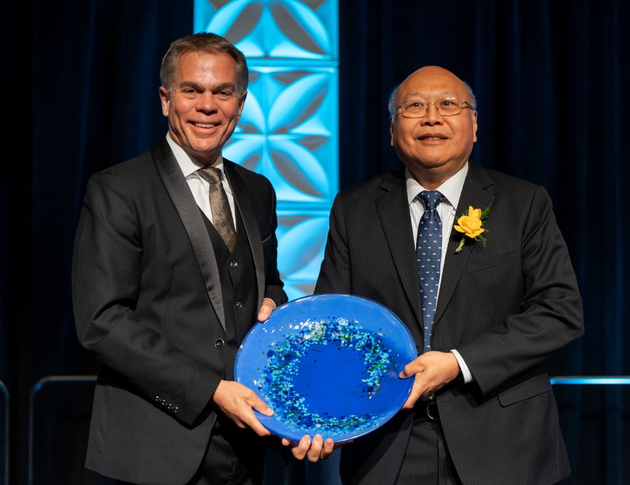 Two men holding a decorative plate at a formal event.