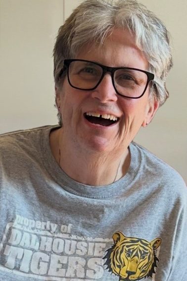 A person with short hair smiles wearing glasses and a Dalhousie Tigers t-shirt.