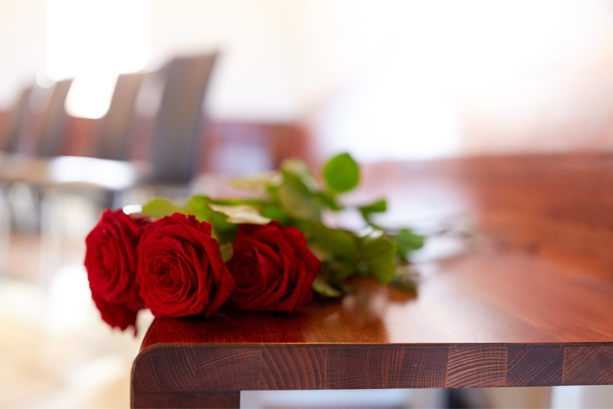 Two red roses sit on a wooden table in front of a row of chairs.