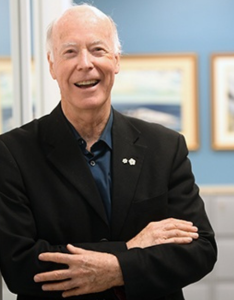 Dr Ronald Stewart is shown from the chest up standing with his arms crossed in a suit jacket and smiling in an indoor setting.