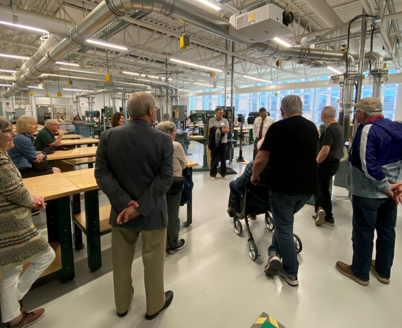 People gathered in a large industrial space listening to and watching a demonstration.