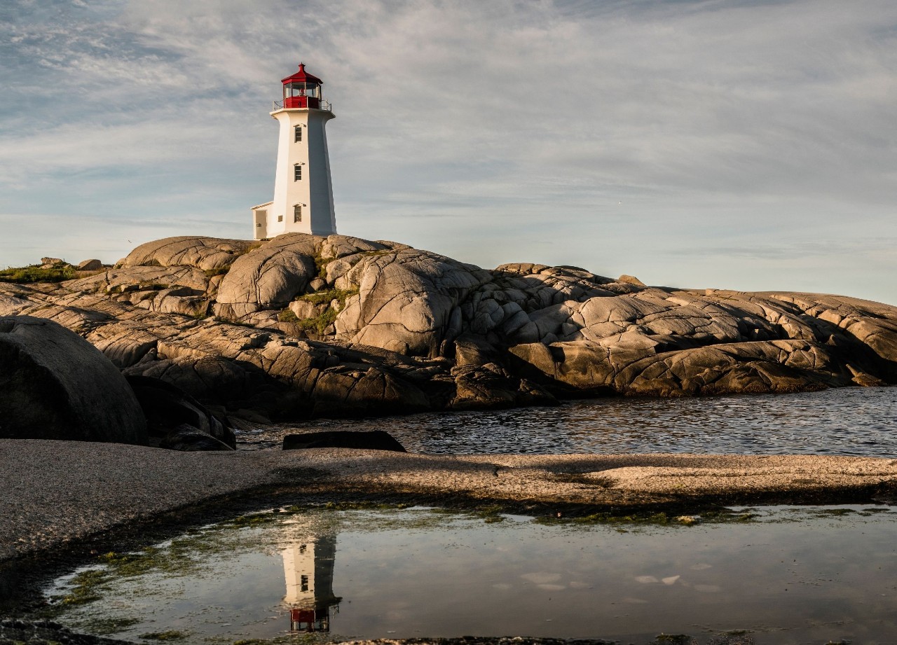 A lighthouse on a rock is reflected in a pooling of water below.