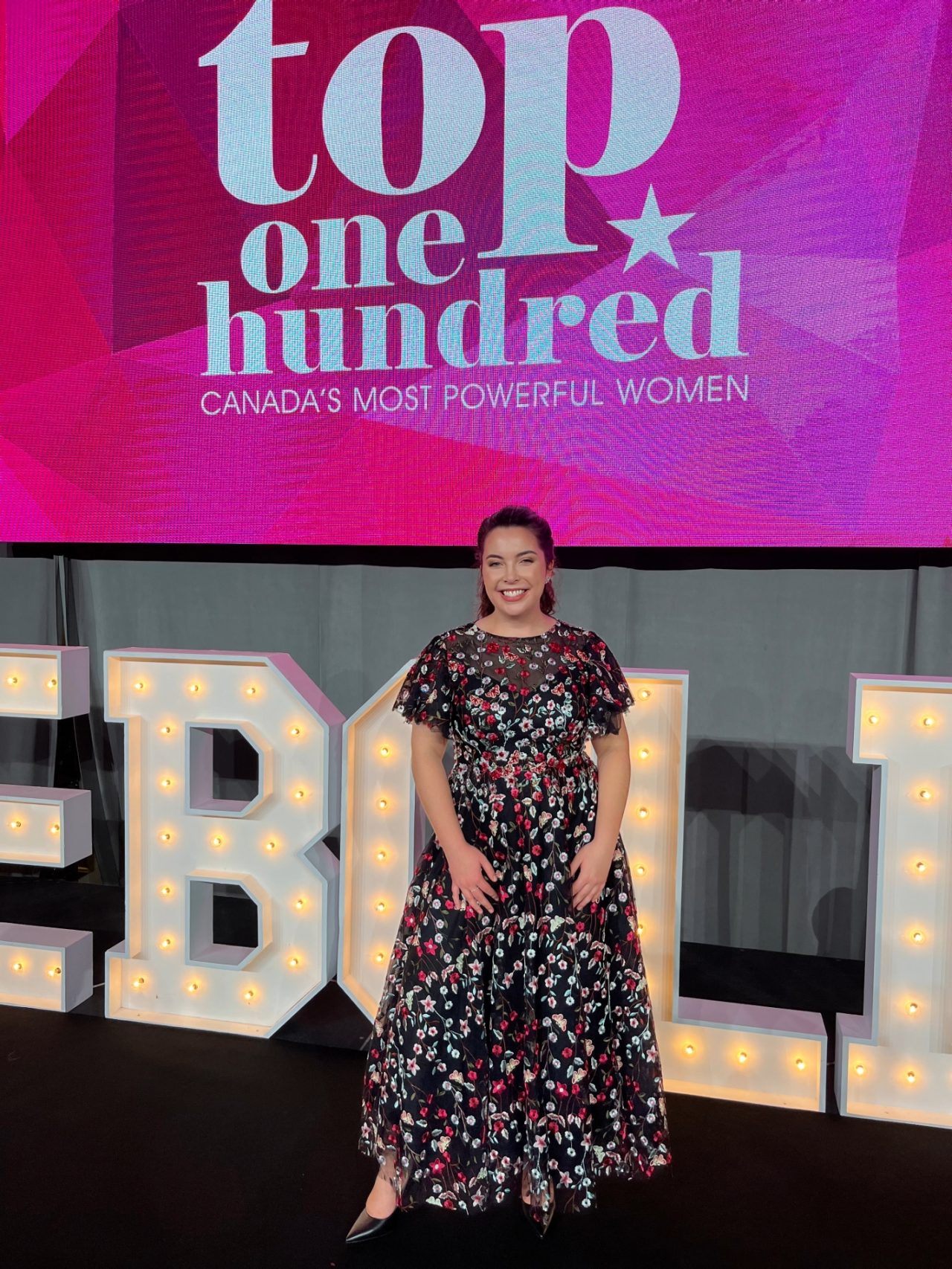 Ollivier posing below a large screen with the event title dressed formally at the event.
