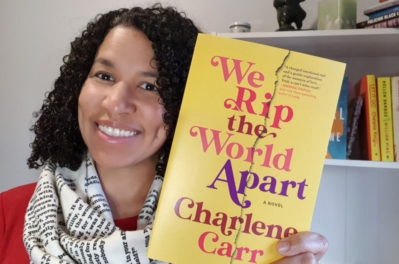 Carr holds up one of her books with a bookshelf in the background.