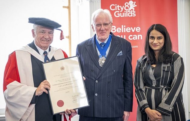 A man in convocation cap and gown holds a framed certificate standing alongside another man and woman.