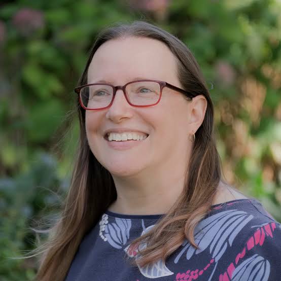 A woman, head and shoulders, wearing glasses smiling in an outdoor setting.