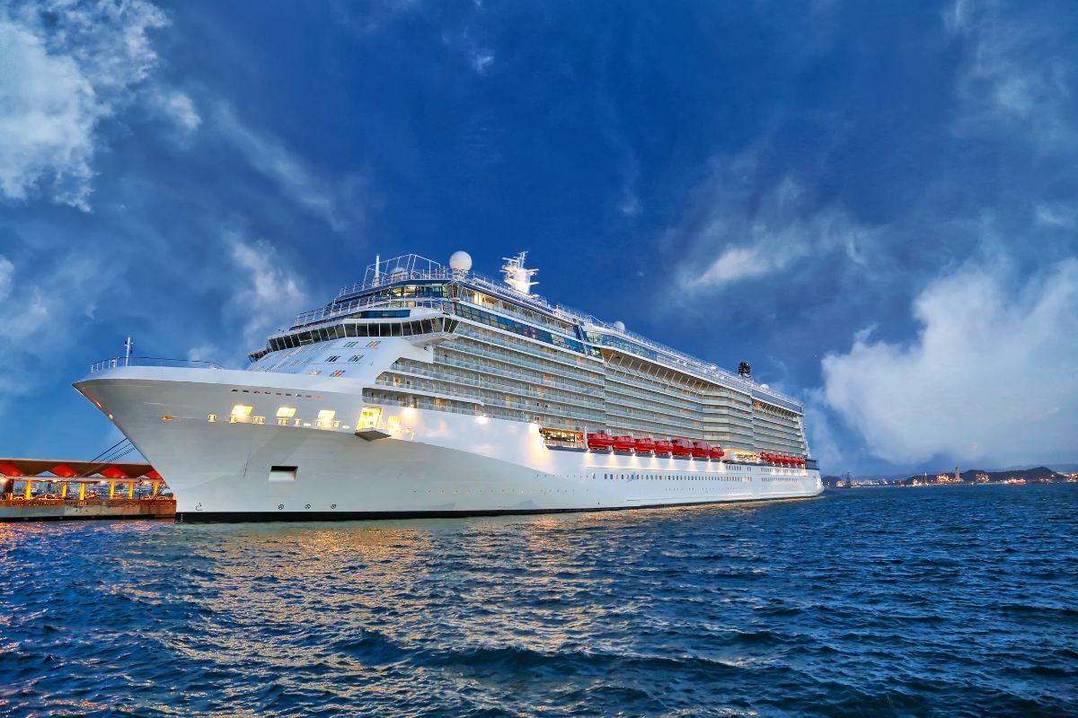 A large cruise ship coming into port under dark blue sky and some clouds.