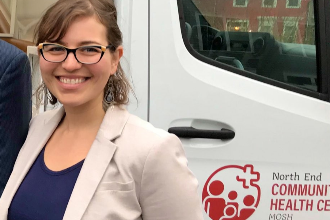A woman dressed in business casual attire smiles alongside a white vehicle with the MOSH logo.