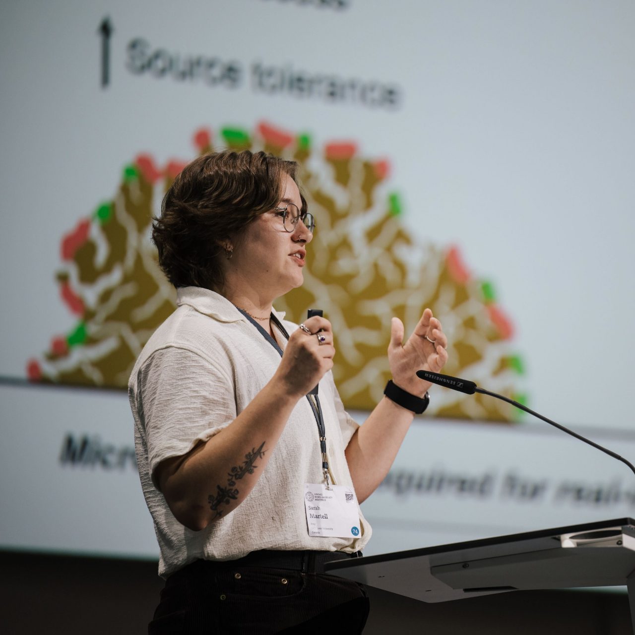 Martell on stage at a podium speaking into a microphone and gesturing with her hands.