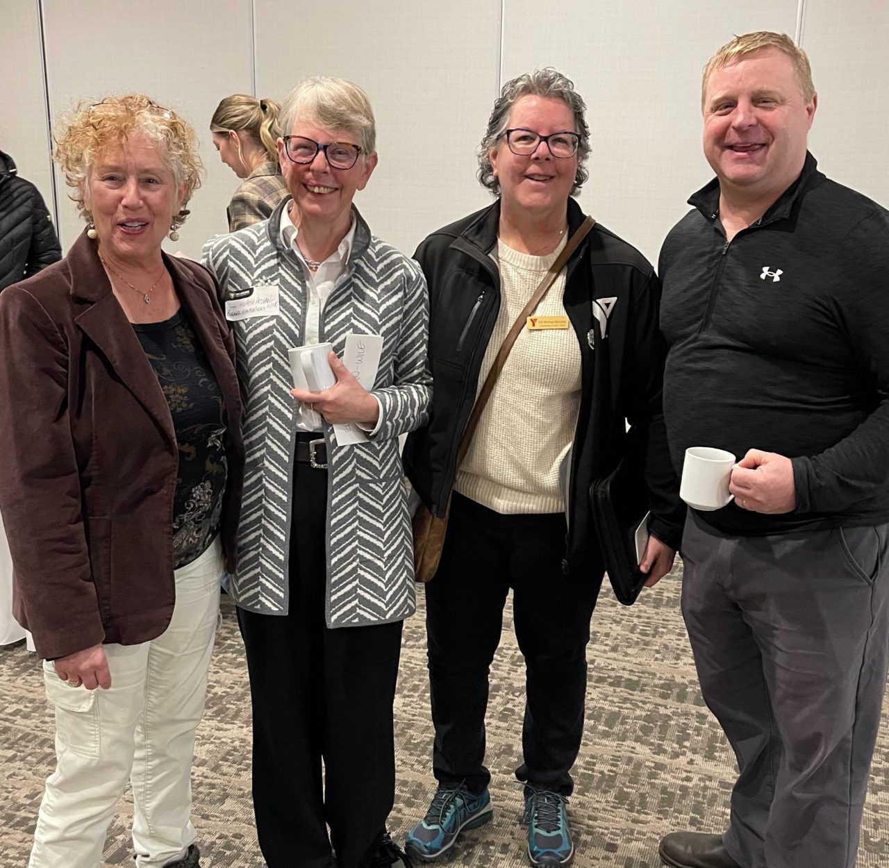 Four people stand together smiling at a casual indoor event.
