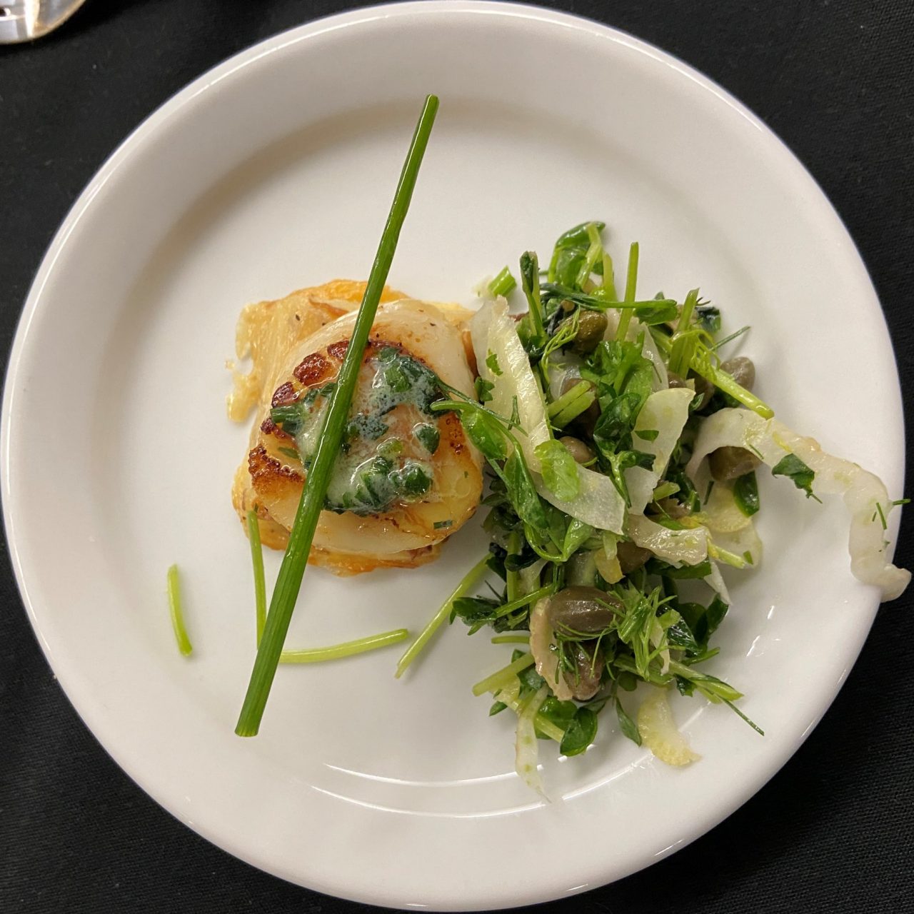 A white plate on a black tablecloth with a mashed potato dish and cooked greens.