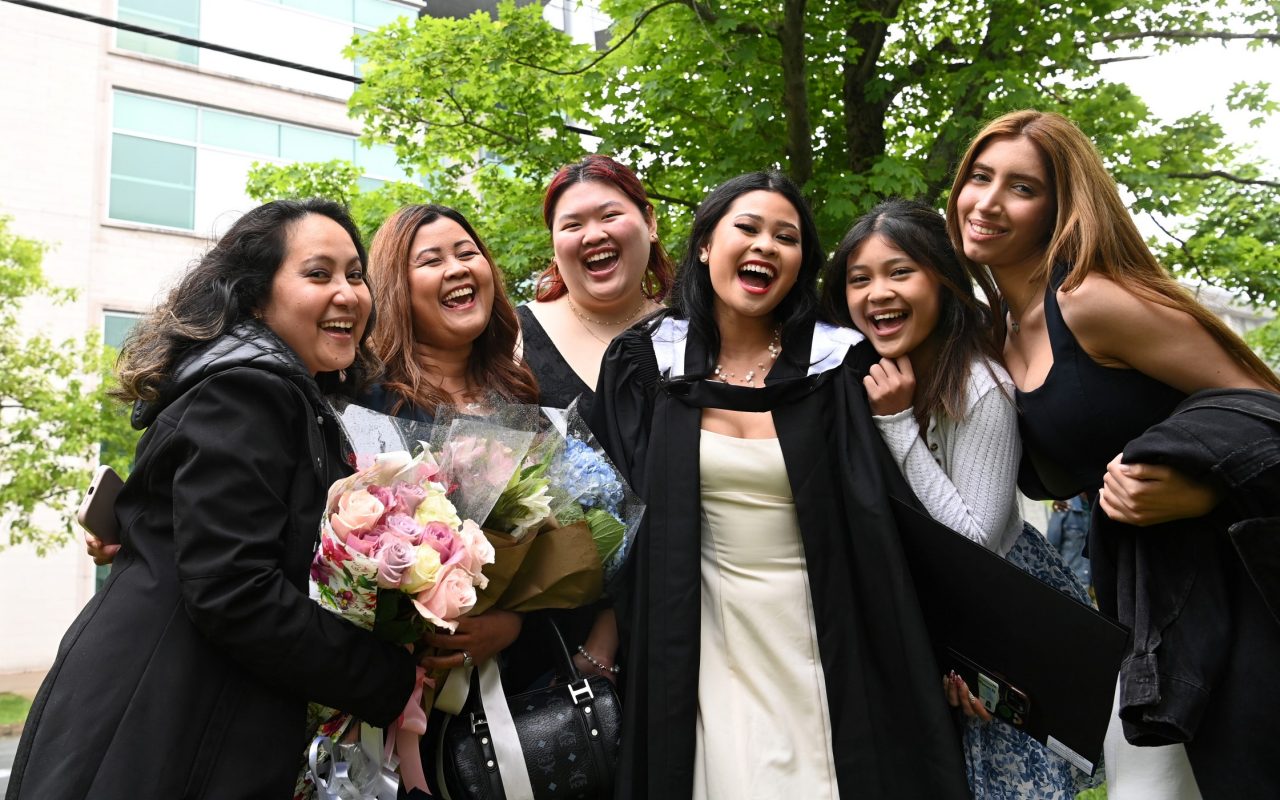A group of women posing for a picture on the street with some holding bouquets of flowers and one in a graduation gown.
