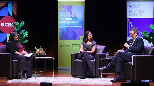 A moderator and two panelists are sitting in lounge chairs on the stage. There are Dalhousie and CBC pull-up banners in the background.
