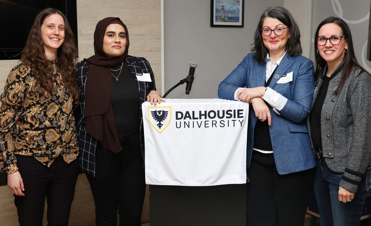 The three women in STEM event speakers and the host standing in front of the podium.