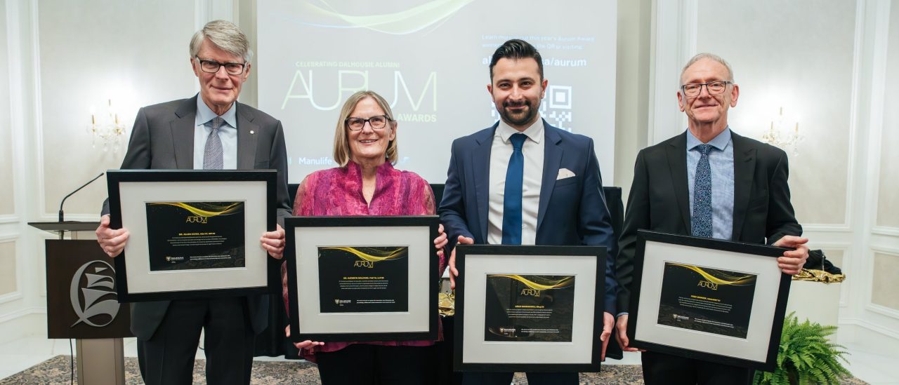 The award recipients stand together displaying their framed award certificates dressed up for the event.