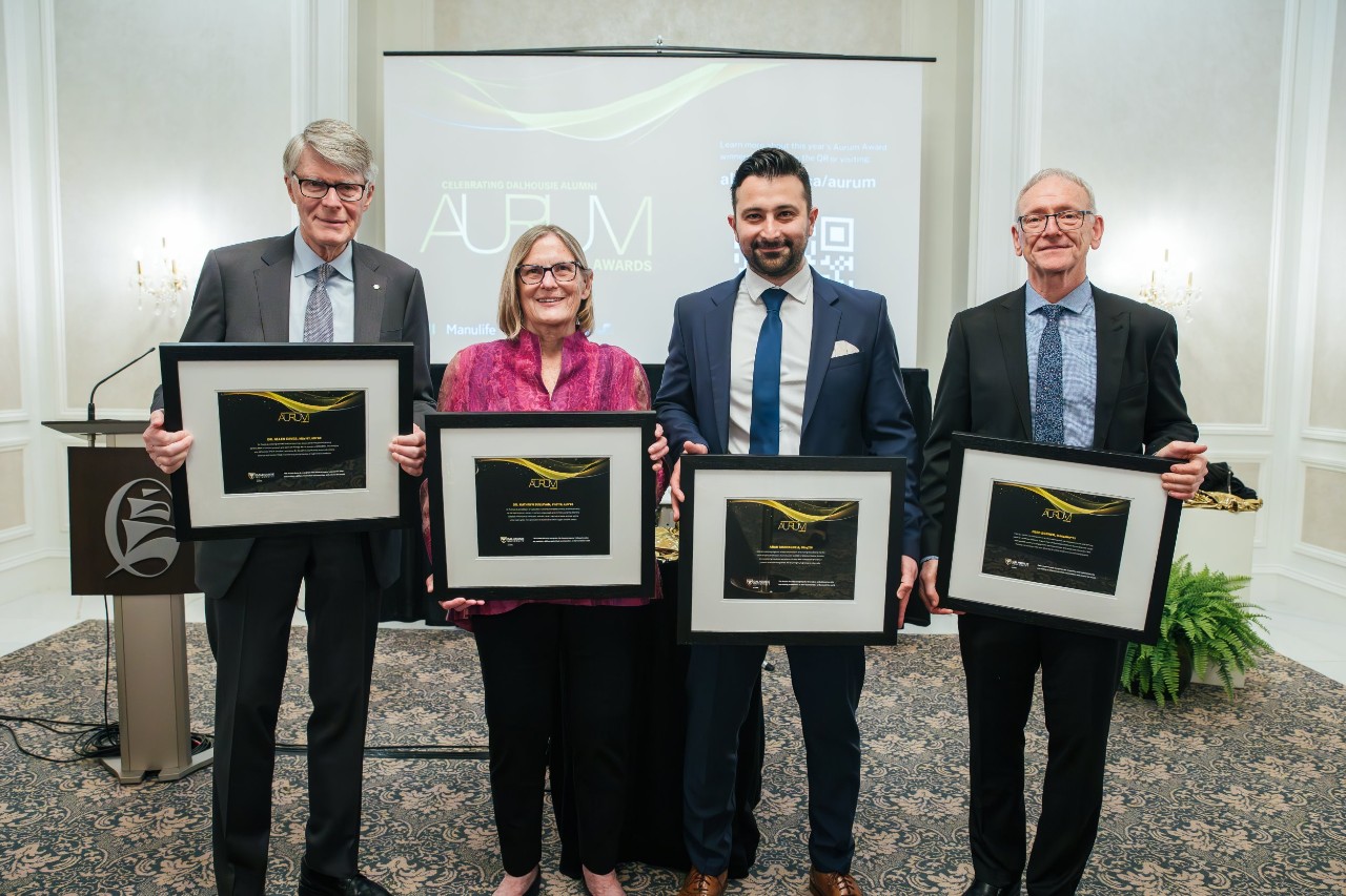 The award recipients stand together displaying their framed award certificates dressed up for the event.
