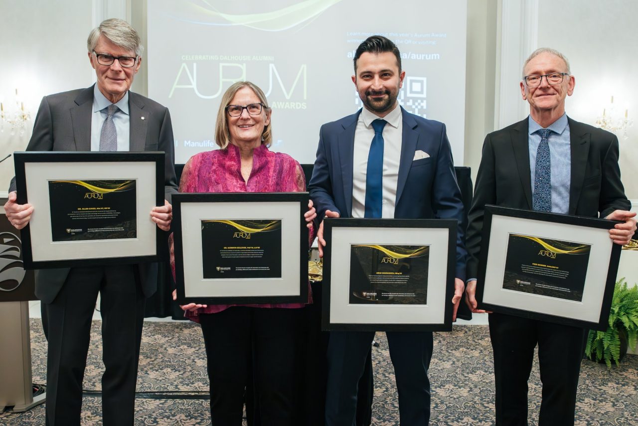 The award recipients stand together displaying their framed award certificates dressed up for the event.