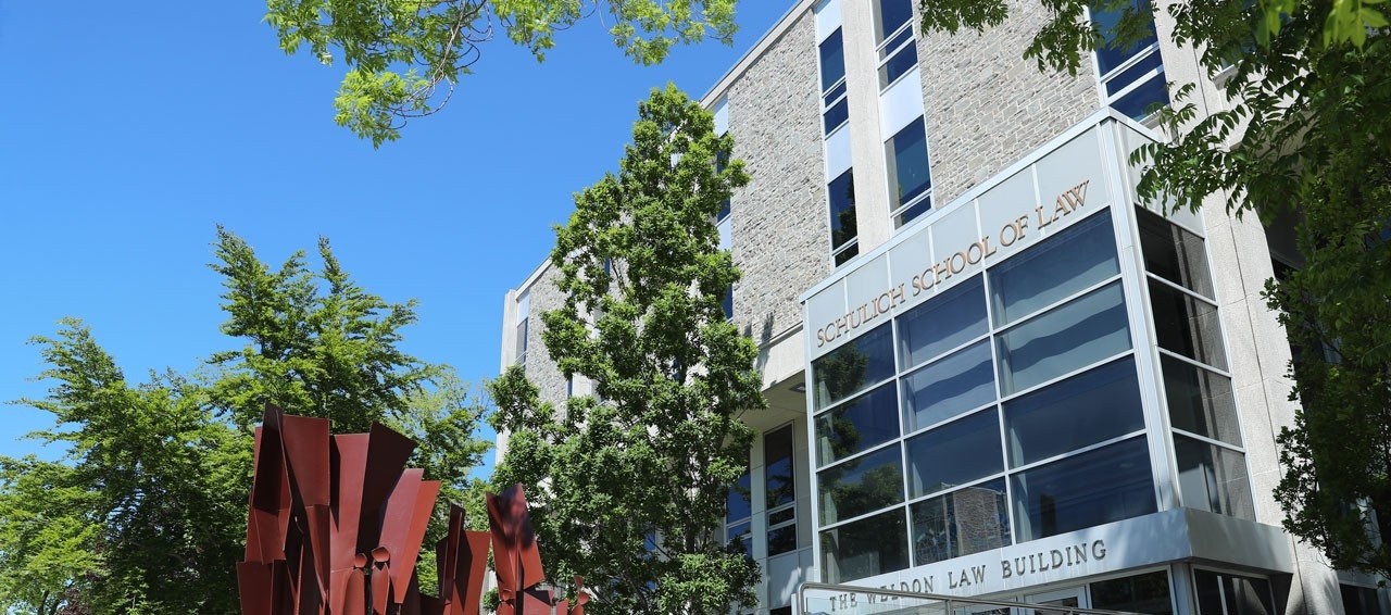 Exterior of the law school building on campus with trees  in leaf and a portion of the art statue out front.