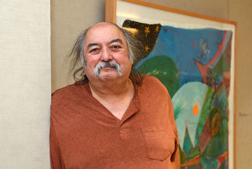 Mi'kmaw artist Alan Syliboy waring a brown shirt stands in front of one of his paintings on display at the Weldon Law Building