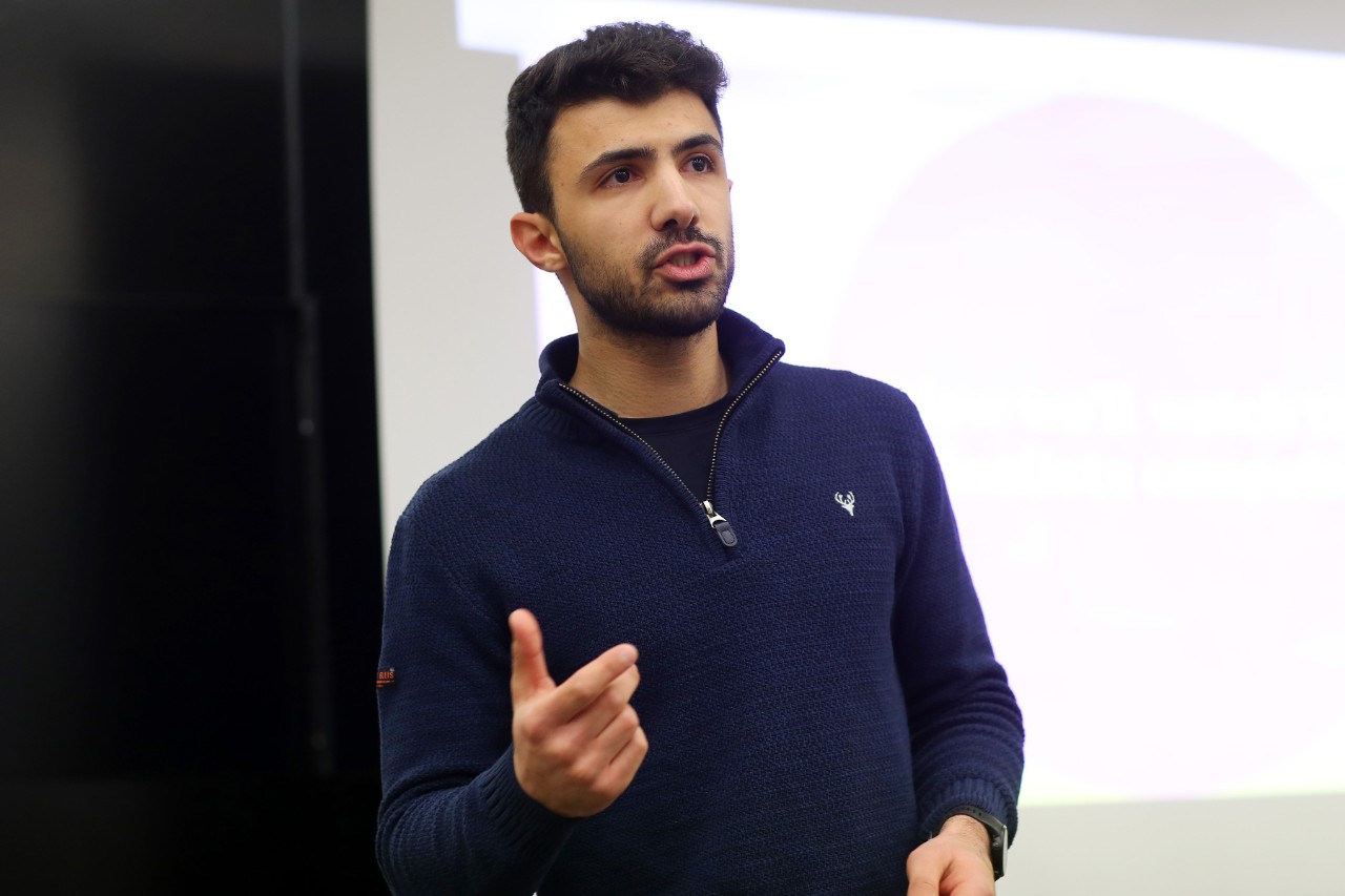 Haddad gestures while presenting in front of a screen.