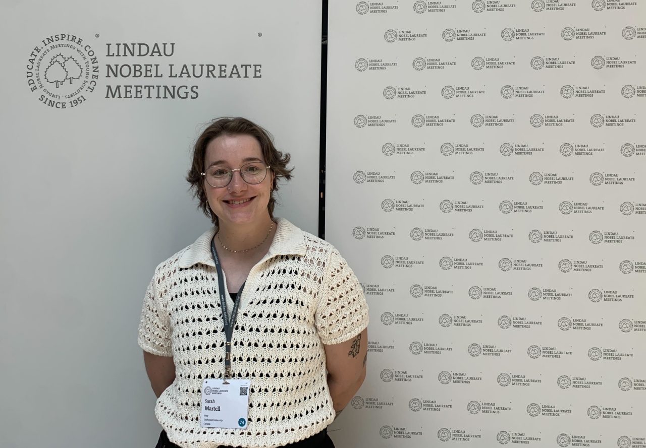 Sarah Martell standing in front of event signage wearing a nametag on a lanyard.
