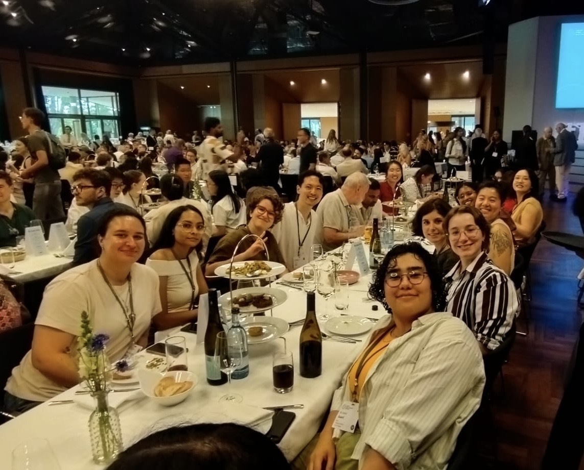 A group of people seated for a casual dinner at a long table in a restaurant among other tables.