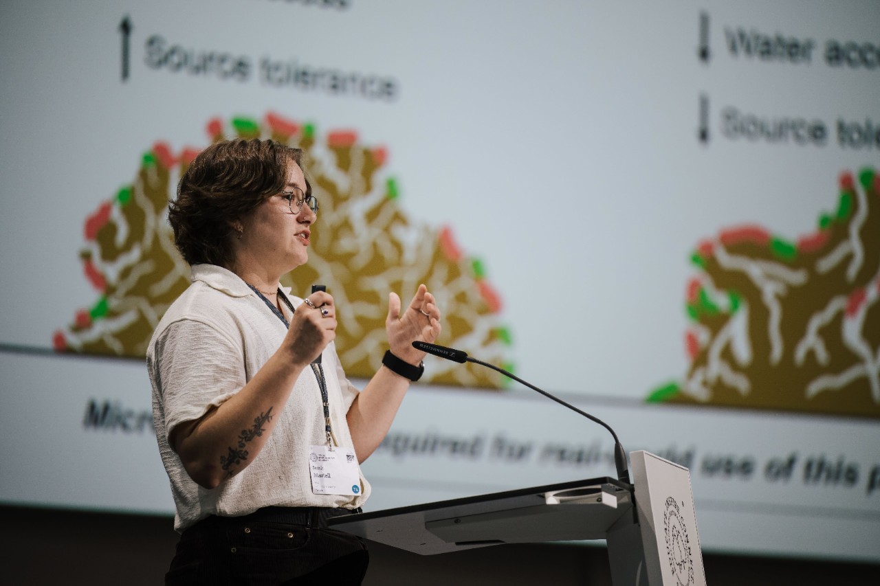 Martell on stage at a podium speaking into a microphone and gesturing with her hands.